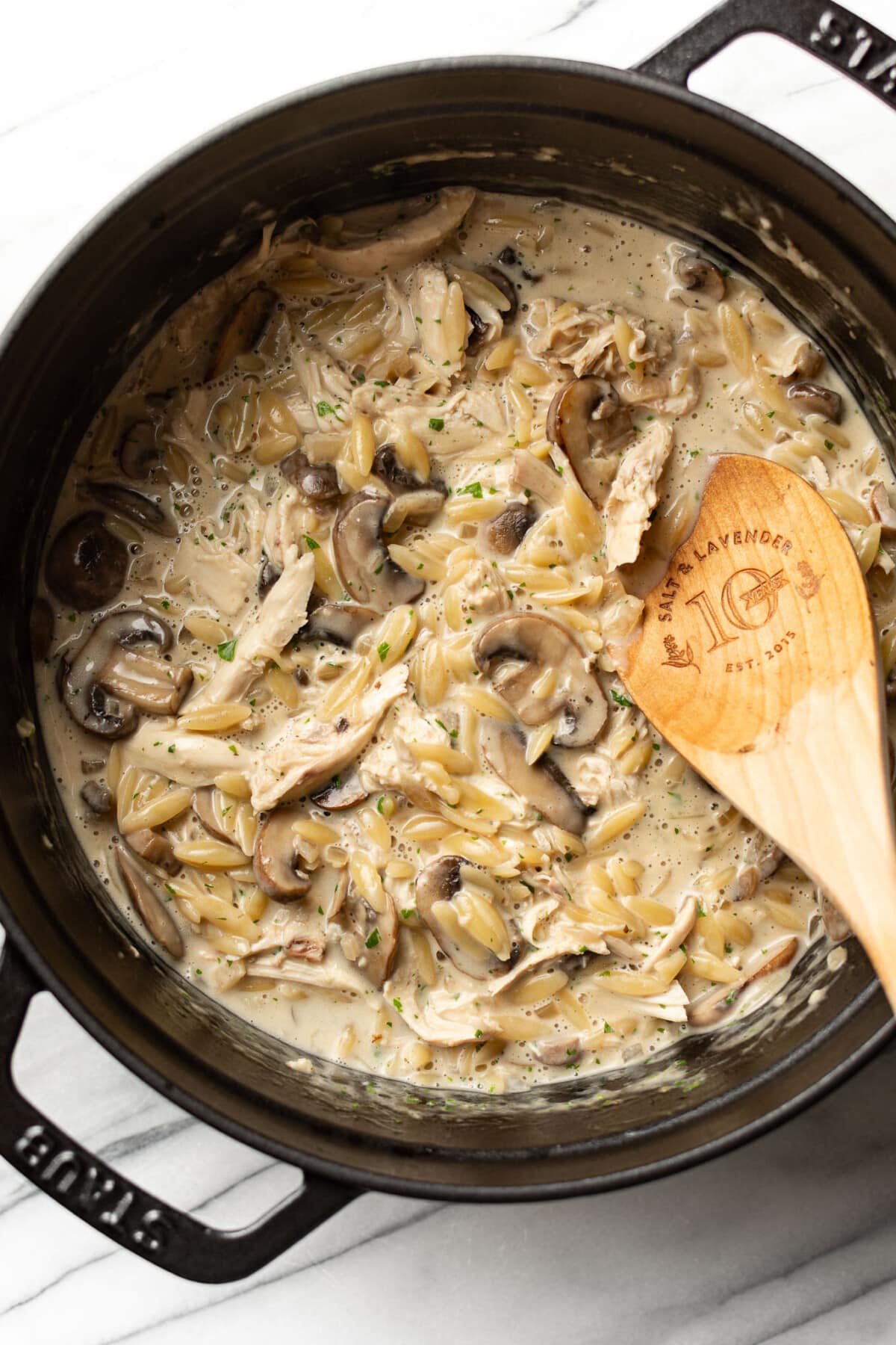 a dutch oven with creamy chicken mushroom orzo and a wooden spoon