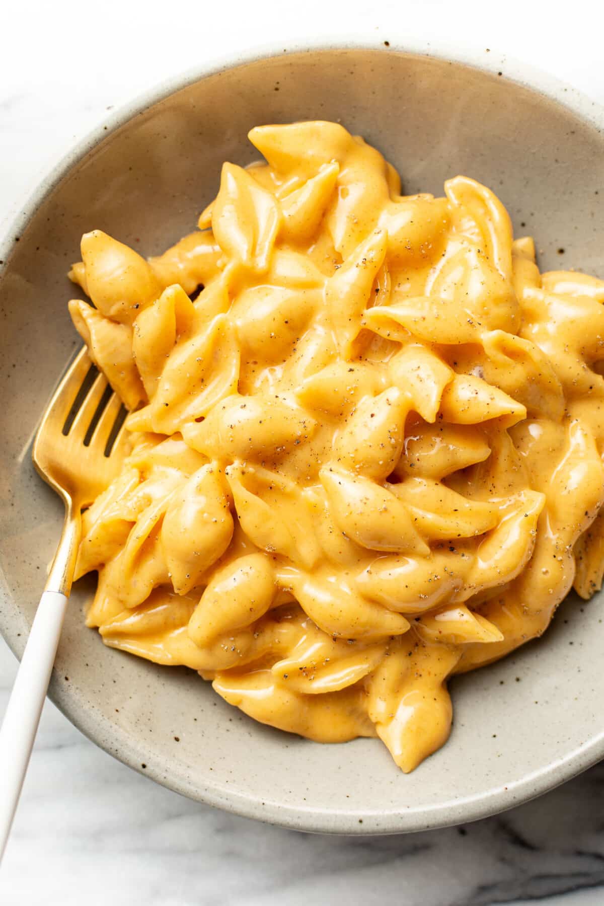 a bowl of cheesy velveeta and shells with a fork