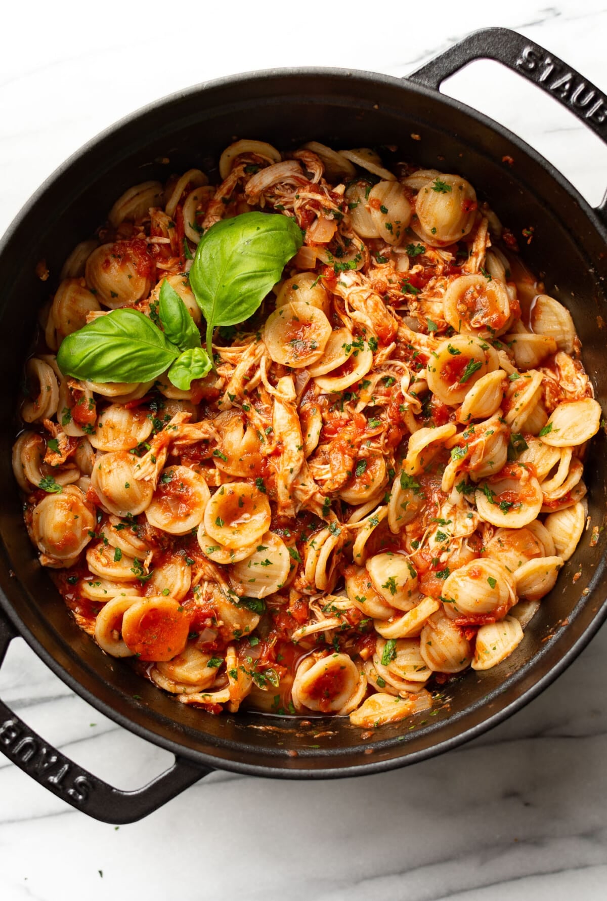a large pot with chicken fra diavolo pasta and a basil sprig