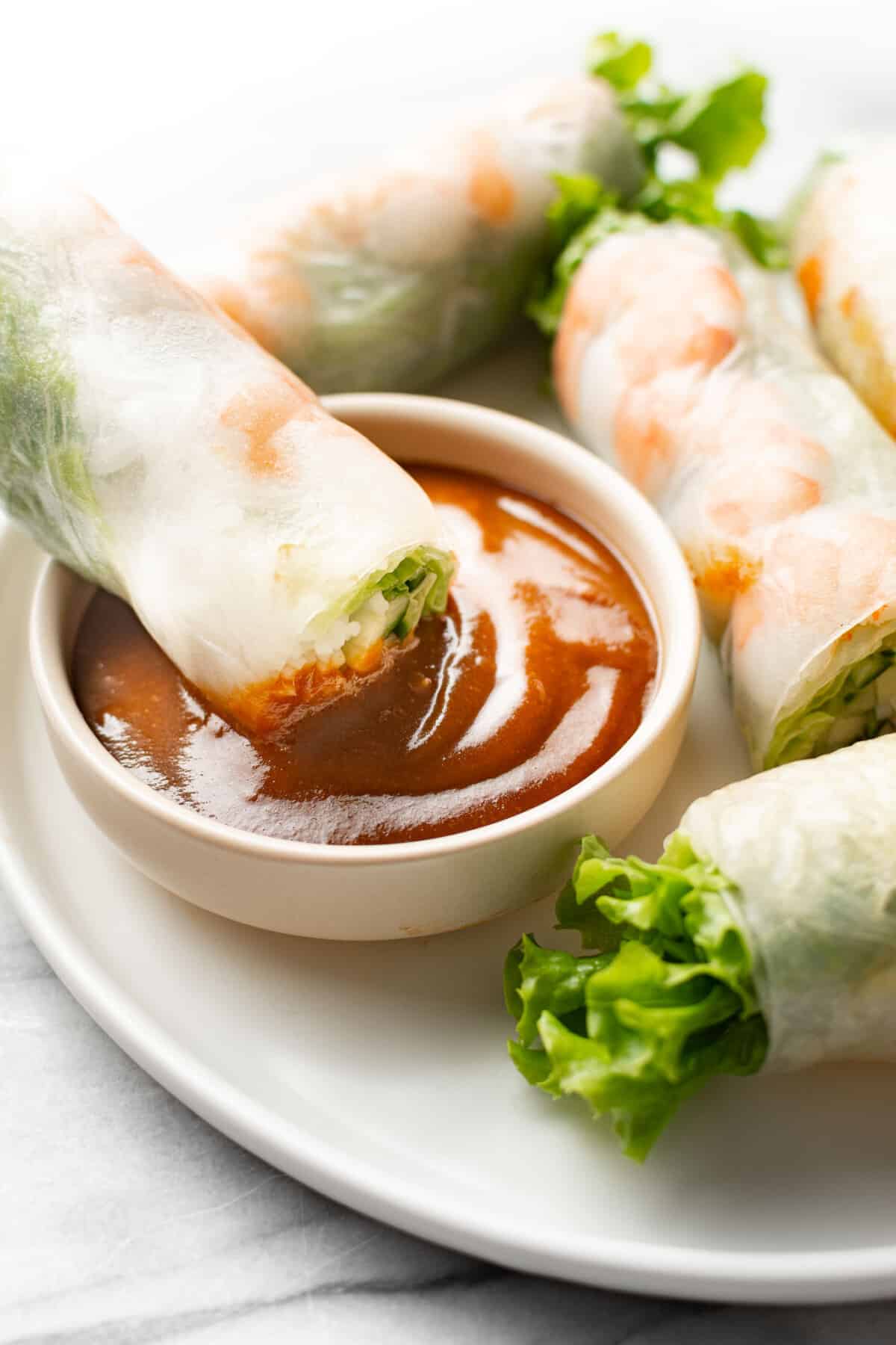 dipping a salad roll into a bowl of peanut sauce