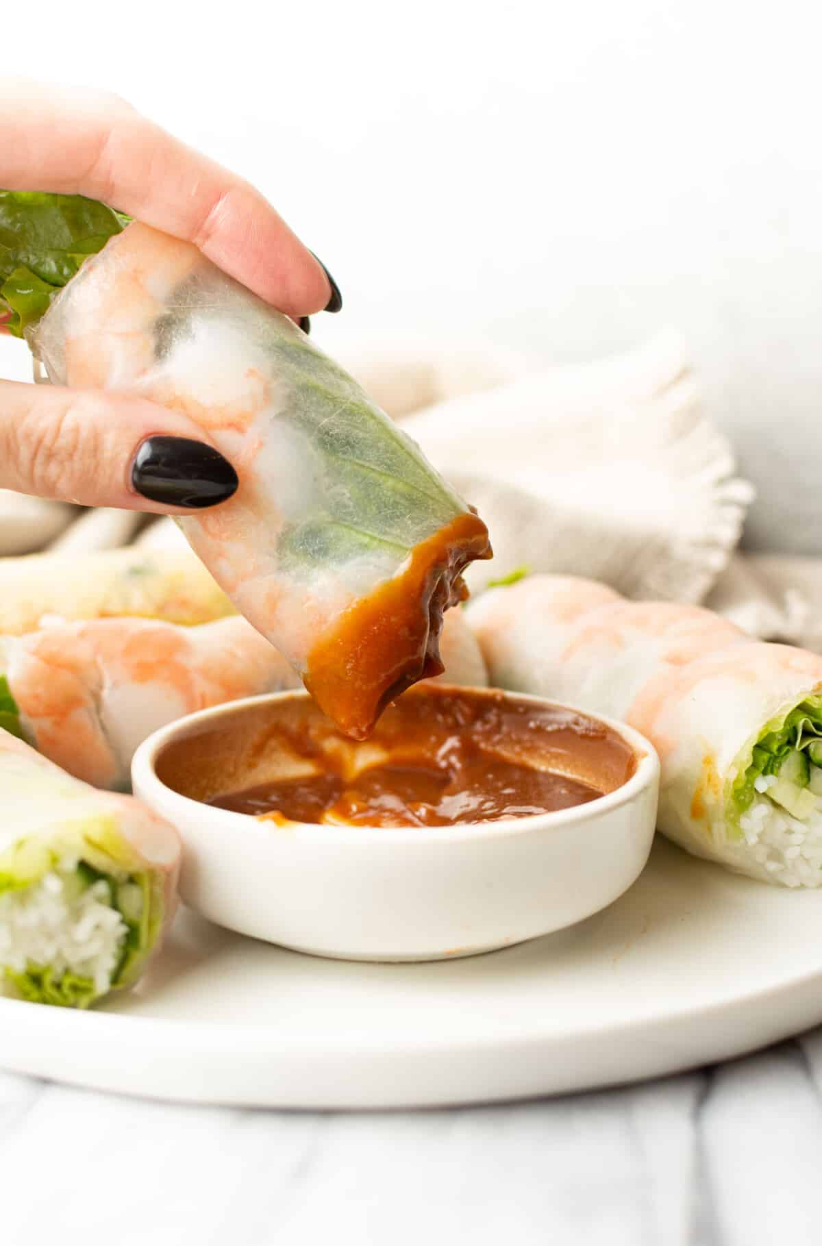 a female hand dipping a salad roll into peanut sauce