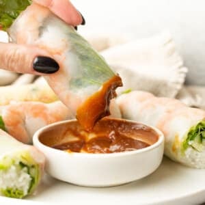 a female hand dipping a salad roll into peanut sauce