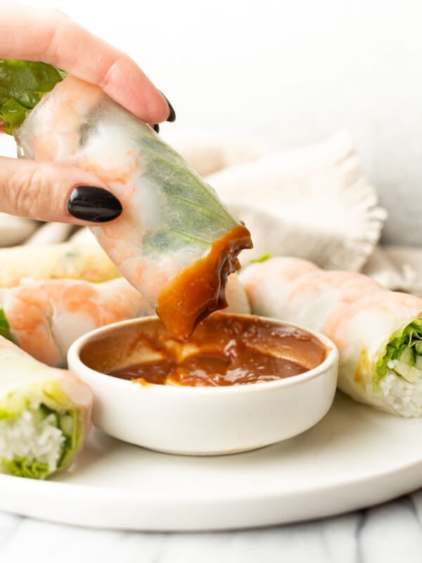 a female hand dipping a salad roll into peanut sauce