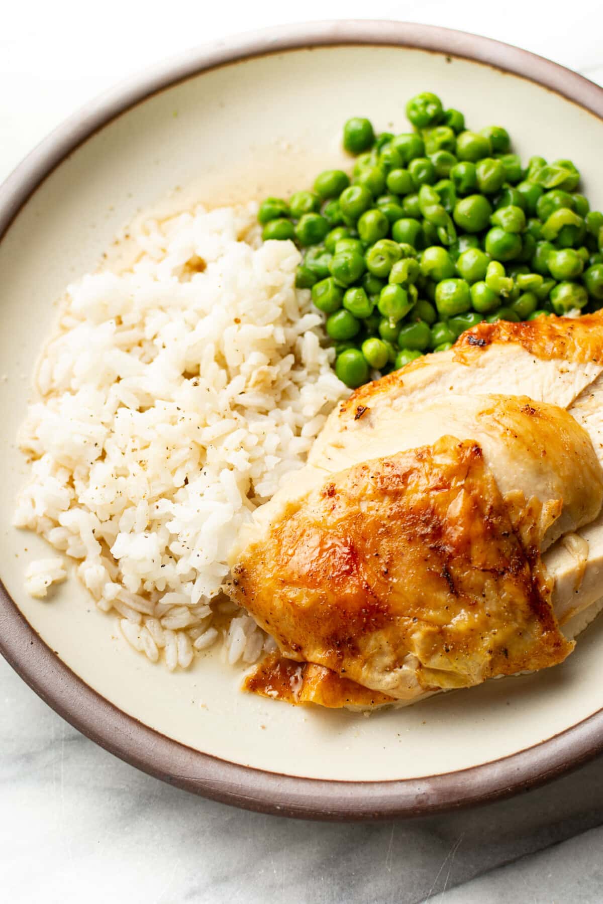 a plate with sliced air fryer roast chicken, peas, and rice