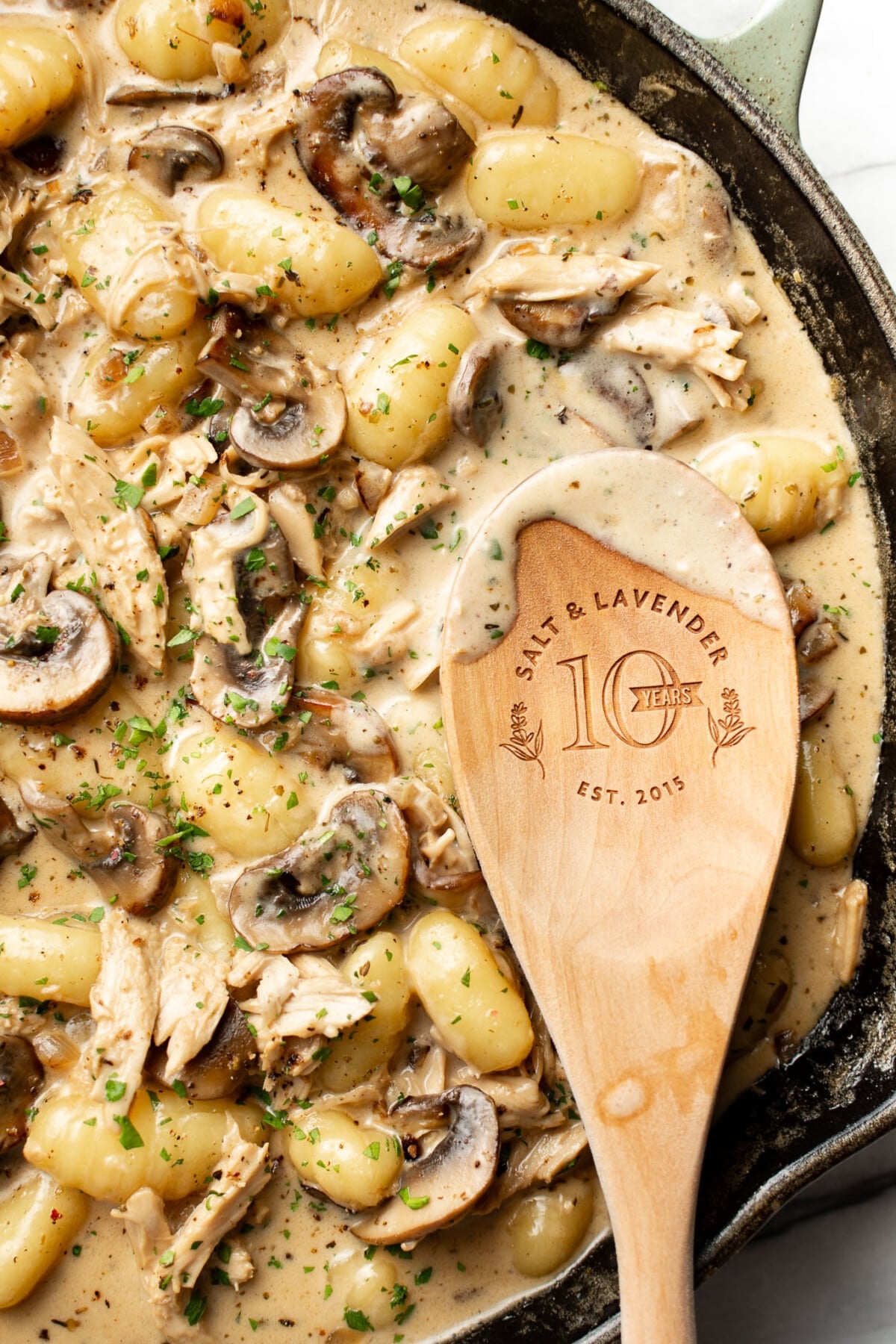 a skillet with chicken mushroom white wine gnocchi and a wooden spoon