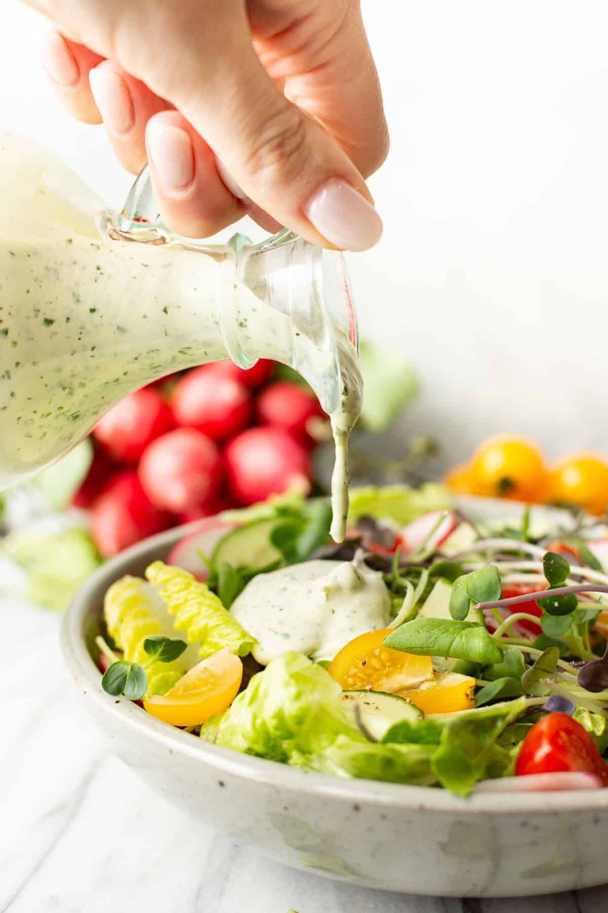 a female hand pouring green goddess dressing onto a bowl of salad