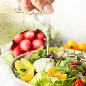 a female hand pouring green goddess dressing onto a bowl of salad