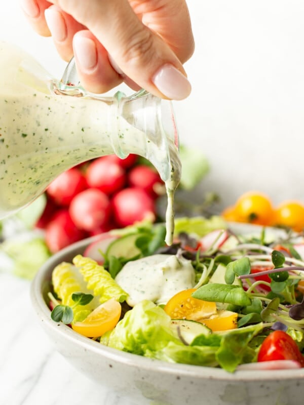 a female hand pouring green goddess dressing onto a bowl of salad