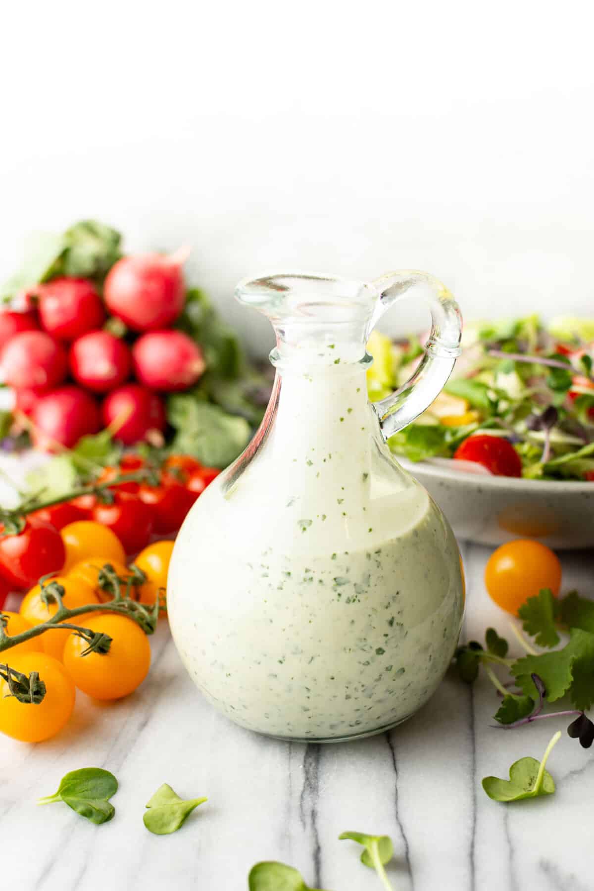a glass container with easy green goddess dressing next to tomatoes on the vine