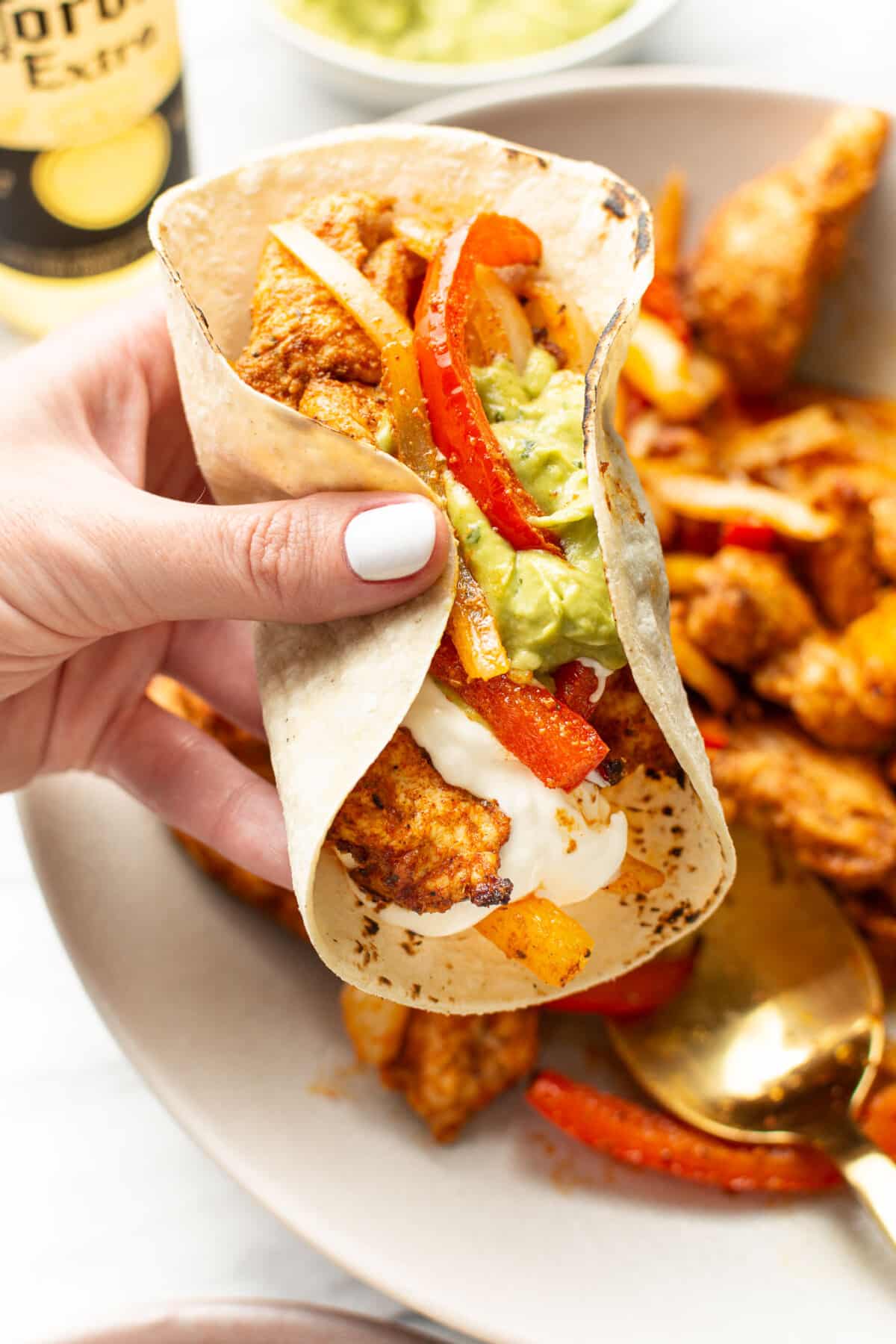 a female hand holding a tortilla with chicken fajitas