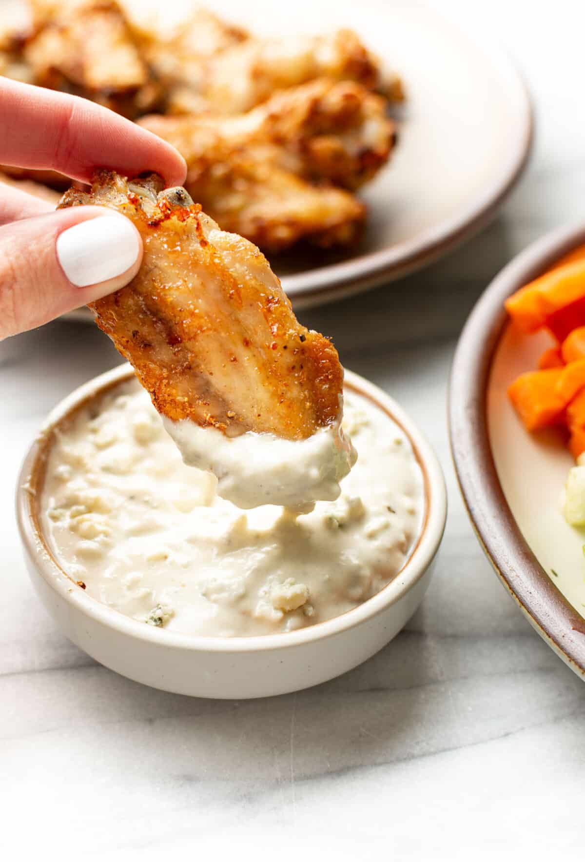 a female hand dipping a chicken wing into blue cheese dressing