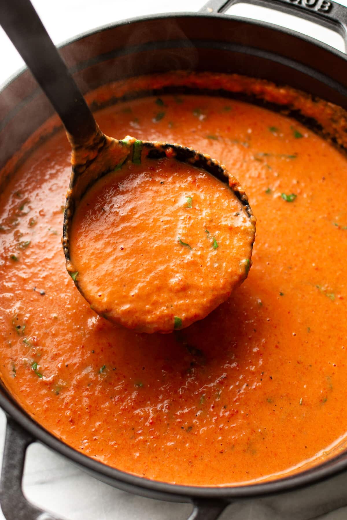 a pot of roasted red pepper soup with a ladle