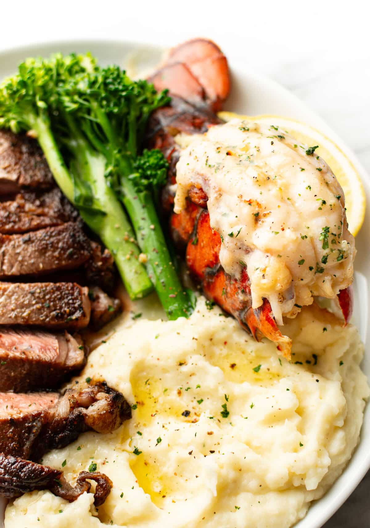 a plate with garlic butter lobster, ribeye steak, mashed potatoes, and broccolini