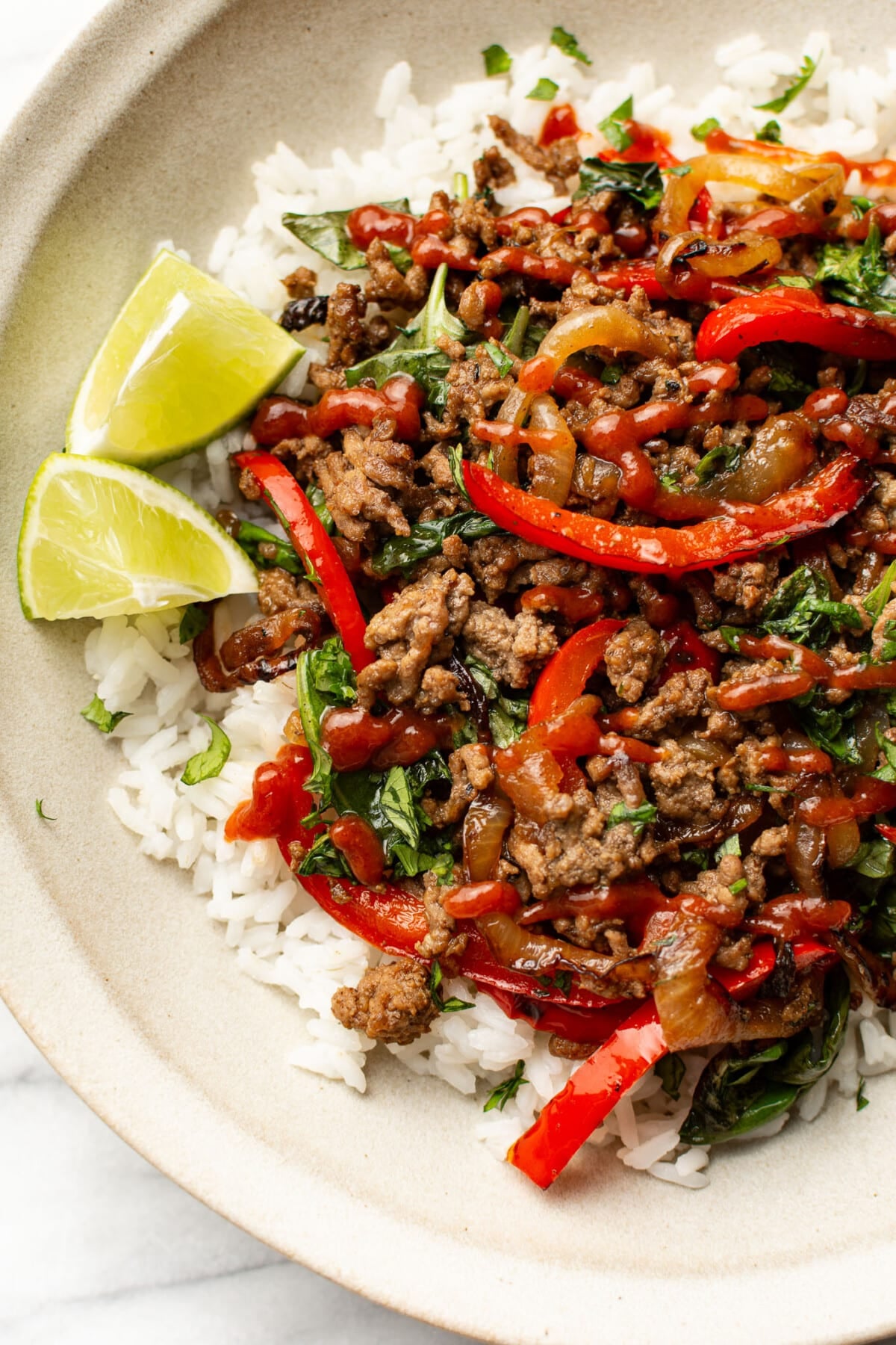 a bowl of thai inspired basil beef over rice with lime wedges