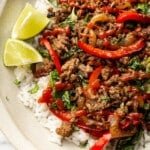 a bowl of thai inspired basil beef over rice with lime wedges