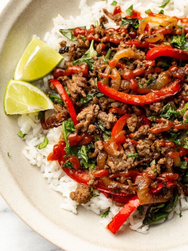 a bowl of thai inspired basil beef over rice with lime wedges